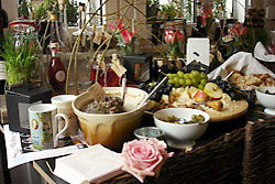 Halb Buffet, halb Stilleben: Tassen, ein Buch, eine Rose, Sch&uuml;sseln, Obst, im Hintergrund Kr&auml;utert&ouml;pfe und Flaschen mit Essig und &Ouml;l