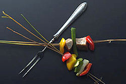 Zwei miteinander gekreuzte Paprika-Fleisch-Spie&szlig;e plus Fleischgabel vor schwarzem Hintergrund