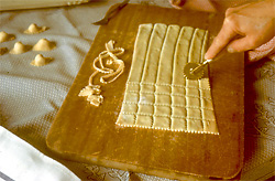 Aus einer Nudelteigplatte r&auml;delt eine Hand auf einem Holzbrett Quadrate f&uuml;r Ravioli aus