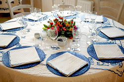 Runder Tisch mit wei&szlig;er Tischdecke, runden blauen Sets, wei&szlig;en Servietten, Gl&auml;sern und Blumenschmuck.